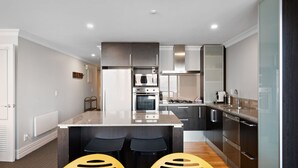 Une cuisine moderne dotée d’un îlot central, d’appareils électroménagers en acier inoxydable et de meubles de cuisine en bois foncé.
