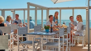 Un área de comedor al aire libre, techada, con mesas y sillas, con vista al mar.