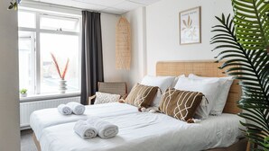 A neatly made double bed with white linens and rolled towels, a woven headboard, and a window with a view of the outside. - Enjoy a relaxing stay in Zoutelande just a 1-minute walk from the beach. This cozy room for 2 offers comfort, coastal charm, and easy access to dunes, seaside cafés, and scenic cycling routes. (Zoutelande)