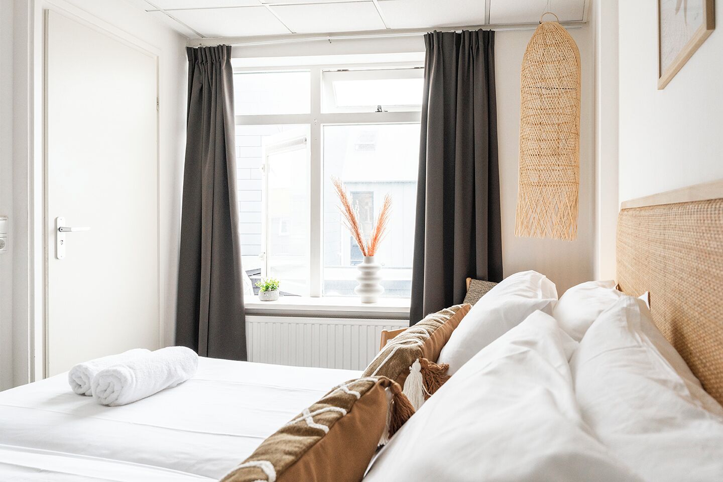 Ein Hotelzimmer mit einem Bett, dunklen Vorhängen, einem Fenster mit Blick und einem gewebten Wandbehang.