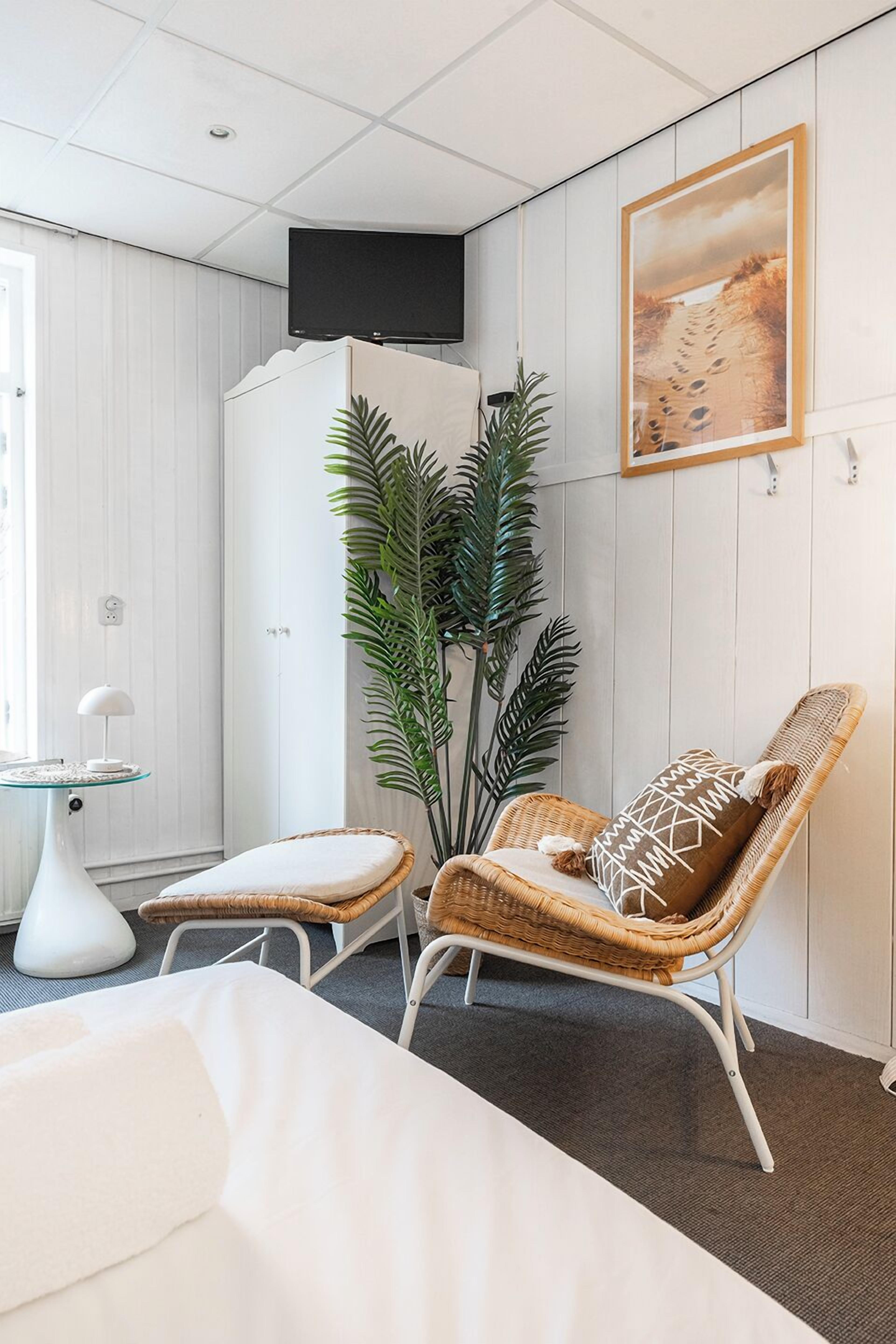 A modern room with a bed, a wicker chair, a small table, a potted plant, and a TV mounted on the wall.
