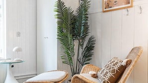 Ein modernes Zimmer mit einem Bett, einem Korbstuhl, einem kleinen Tisch, einer Topfpflanze und einem an der Wand befestigten Fernseher.