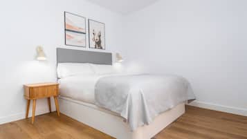 A modern bedroom with a bed, wooden bedside tables, wall-mounted lamps, and two framed pictures.