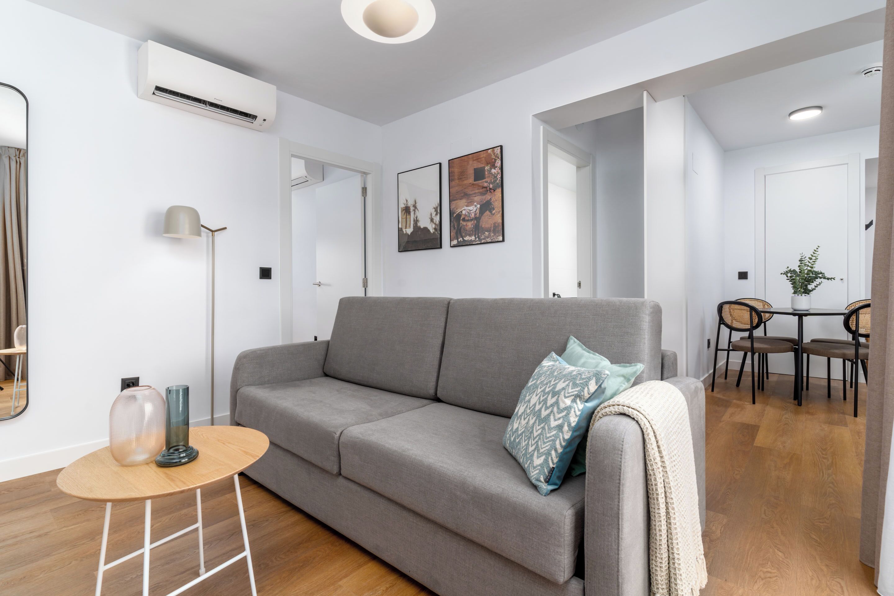 A modern living room with a grey sofa, a small wooden table, and a dining area with a table and chairs.