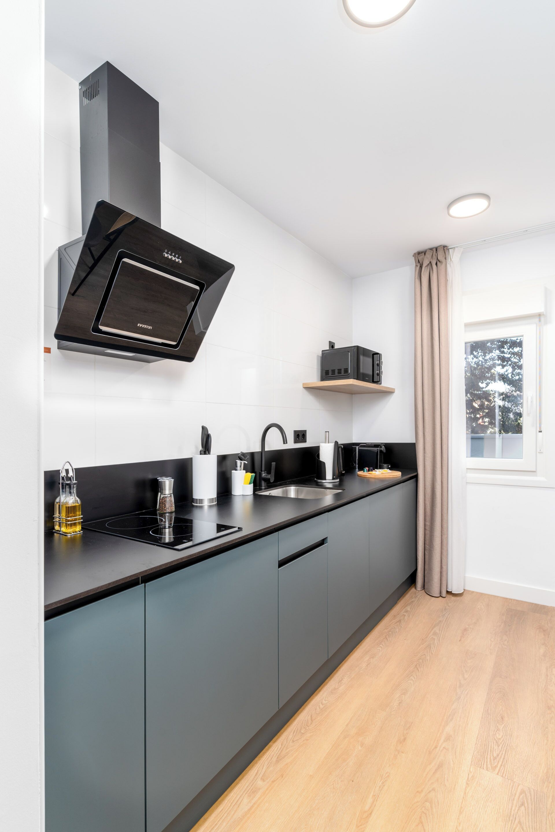 A modern kitchen with grey cabinets, a black range hood, and a window with a view of trees.