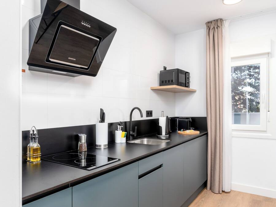 Una cocina moderna con armarios grises, una campana extractora negra y un ventanal con vistas a árboles.