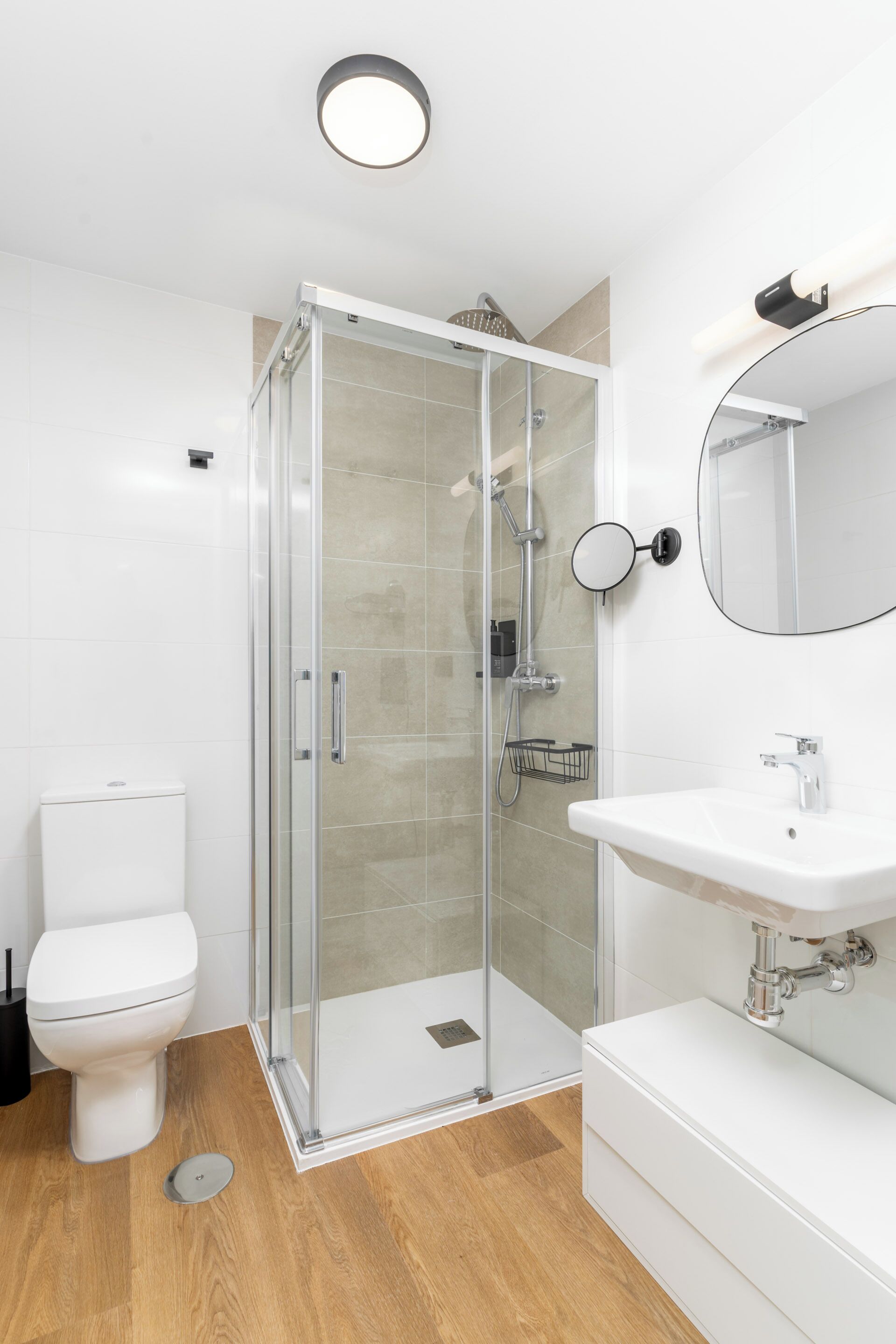 Un baño moderno con cabina de ducha de vidrio, inodoro blanco y lavamanos con espejo.