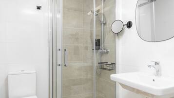 A modern bathroom with a glass shower enclosure, a white toilet, and a sink with a mirror.