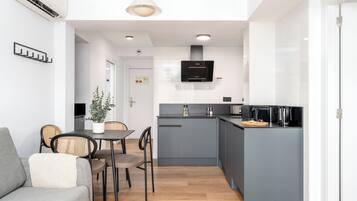 A compact kitchen with grey cabinets, a built-in oven, and a small island with a kettle.