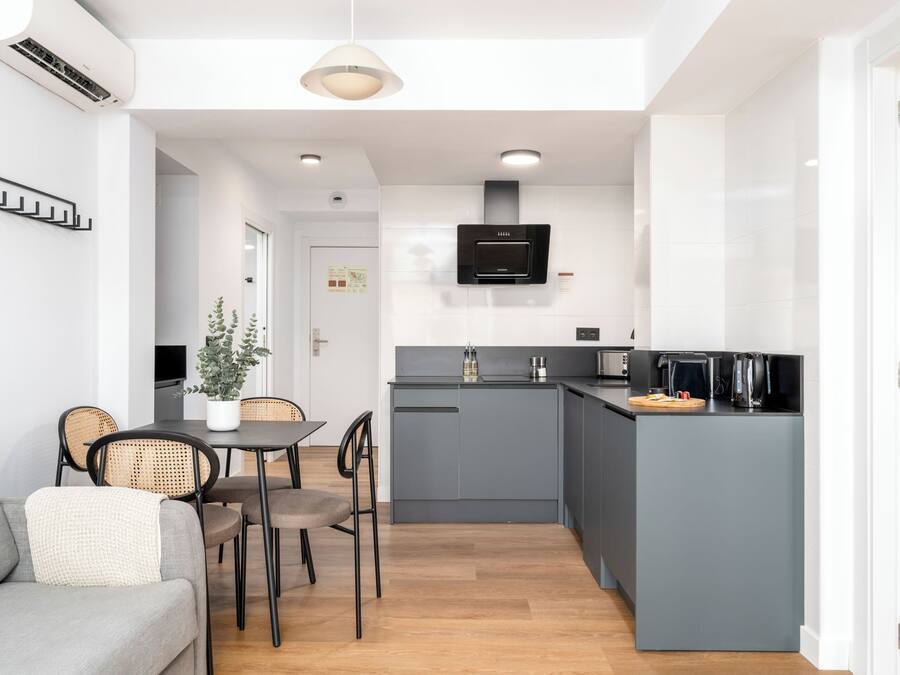 A compact kitchen with grey cabinets, a built-in oven, and a small island with a kettle.