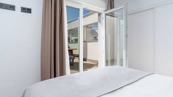 Una habitación de hotel con cama, puerta corrediza de vidrio hacia un espacio exterior y una pequeña mesa con sillas.