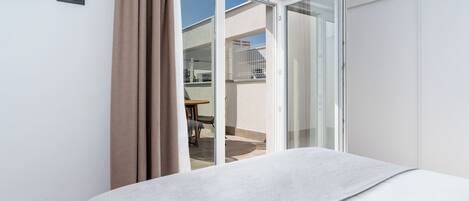 Una habitación de hotel con cama, puerta corrediza de vidrio hacia un espacio exterior y una pequeña mesa con sillas.