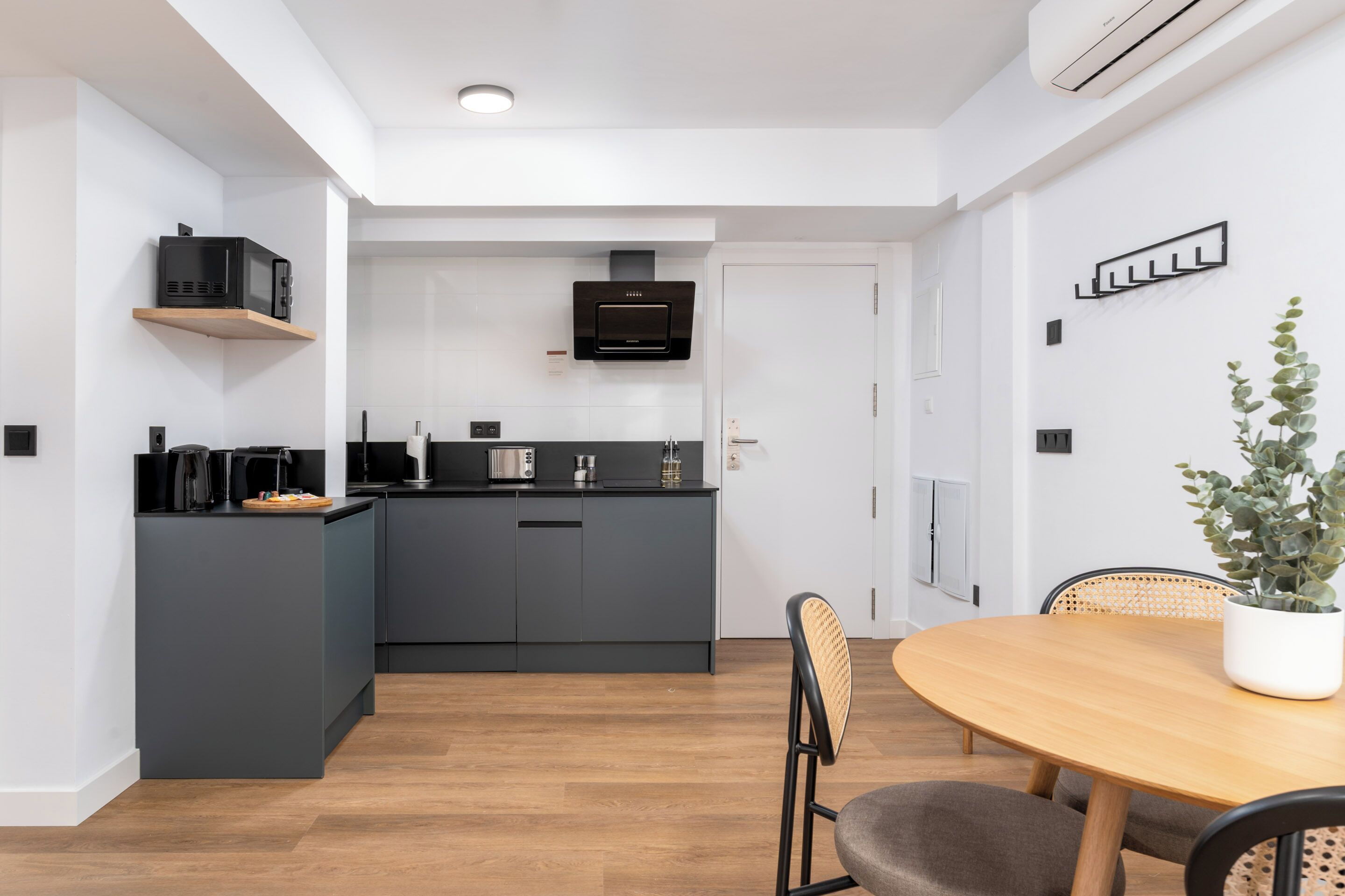 A modern kitchen with dark cabinetry, a microwave, and a built-in oven. There is a dining area with a wooden table and chairs.