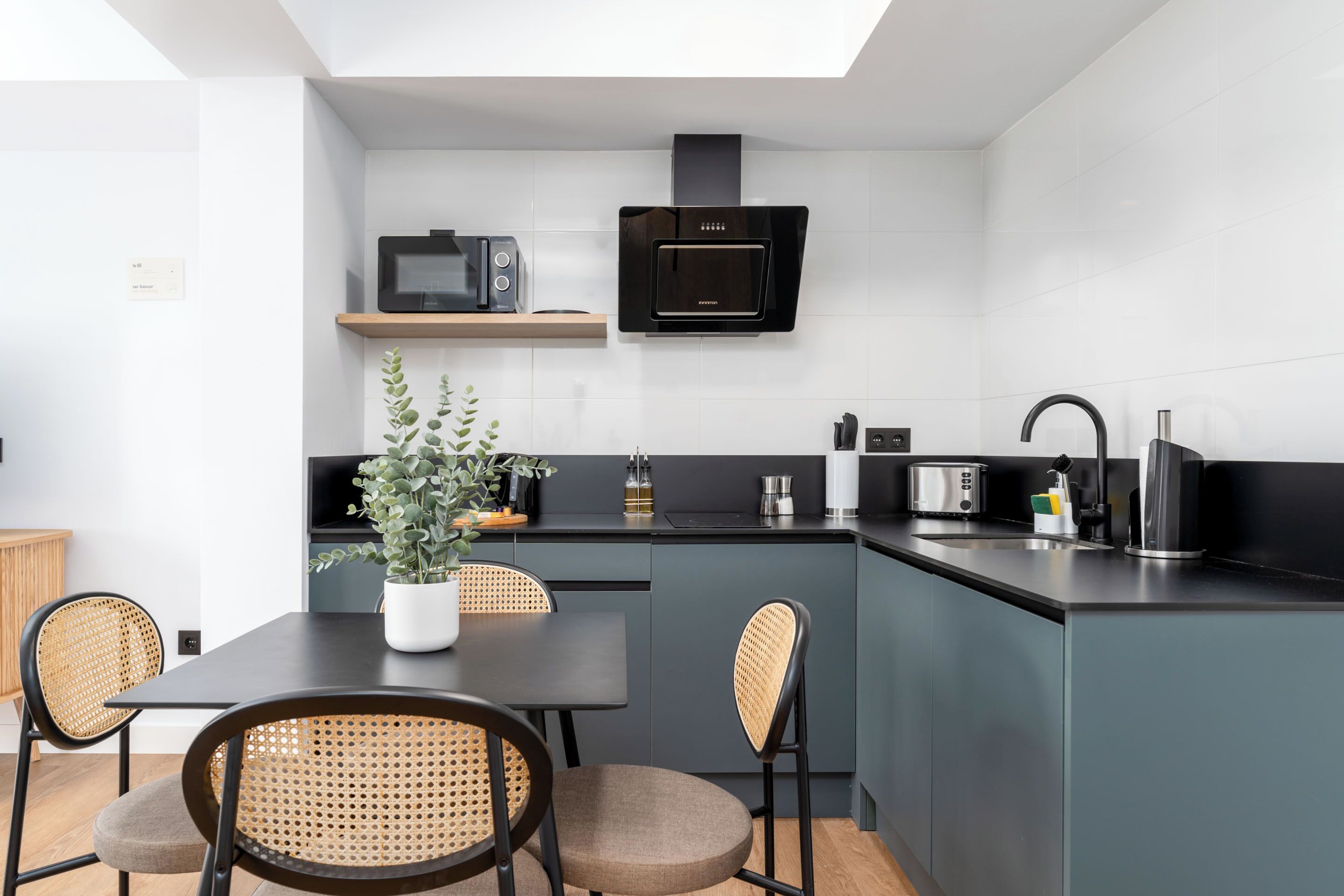 A modern kitchen with a built-in microwave, oven, and sink. There is a dining table with chairs and a potted plant.