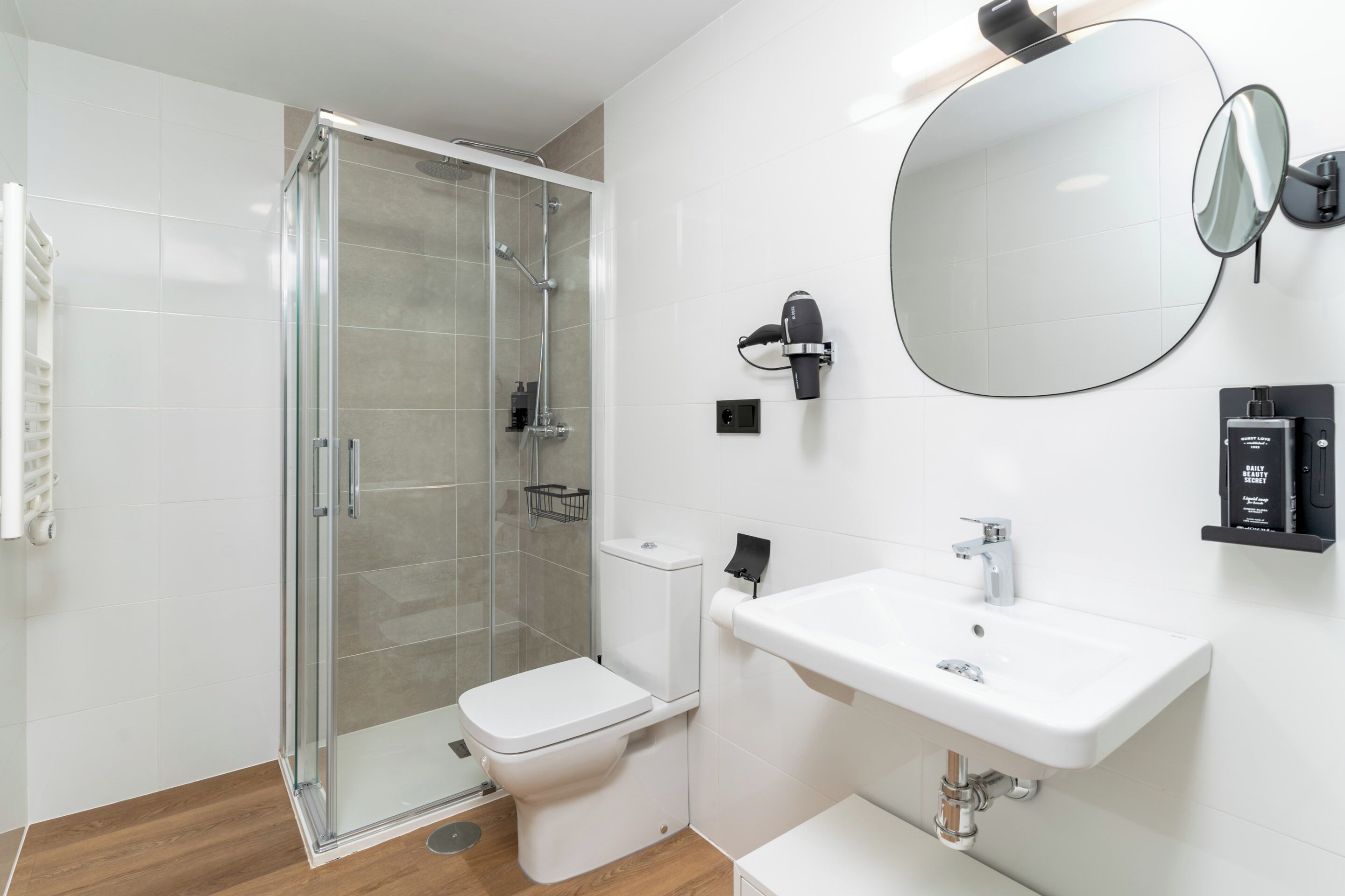 Une salle de bain moderne avec une douche à parois de verre, des toilettes blanches, un lavabo avec un miroir et un porte-serviettes.
