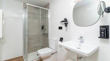 A modern bathroom with a glass-enclosed shower, a white toilet, a sink with a mirror, and a towel rack.