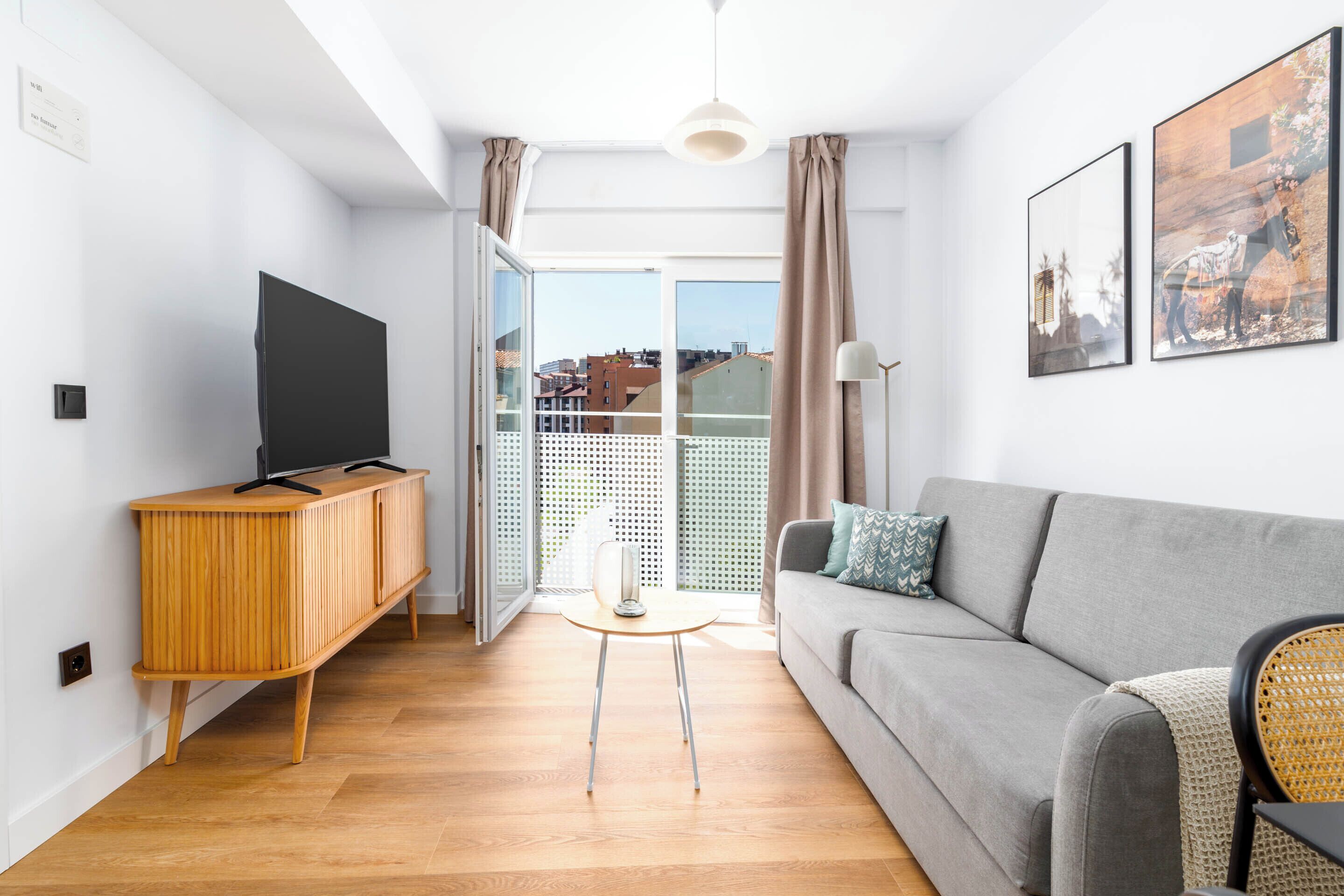 A modern living room with a grey sofa, wooden cabinet, and a flat-screen TV.