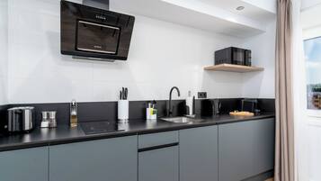 A modern kitchen with grey cabinets, a black countertop, a built-in oven, a microwave, and a window with curtains.