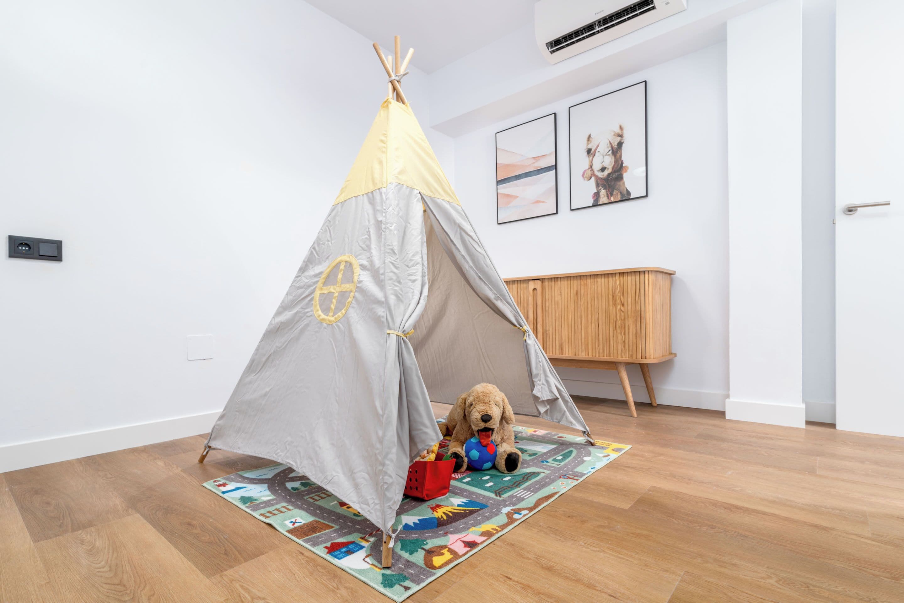 Quarto com piso de madeira, parede branca, armário de madeira e uma tenda com um cachorro de brinquedo dentro.