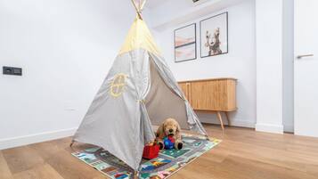 Una habitación con piso de madera, pared blanca, un armario de madera y una tienda de campaña con un perro de juguete dentro.