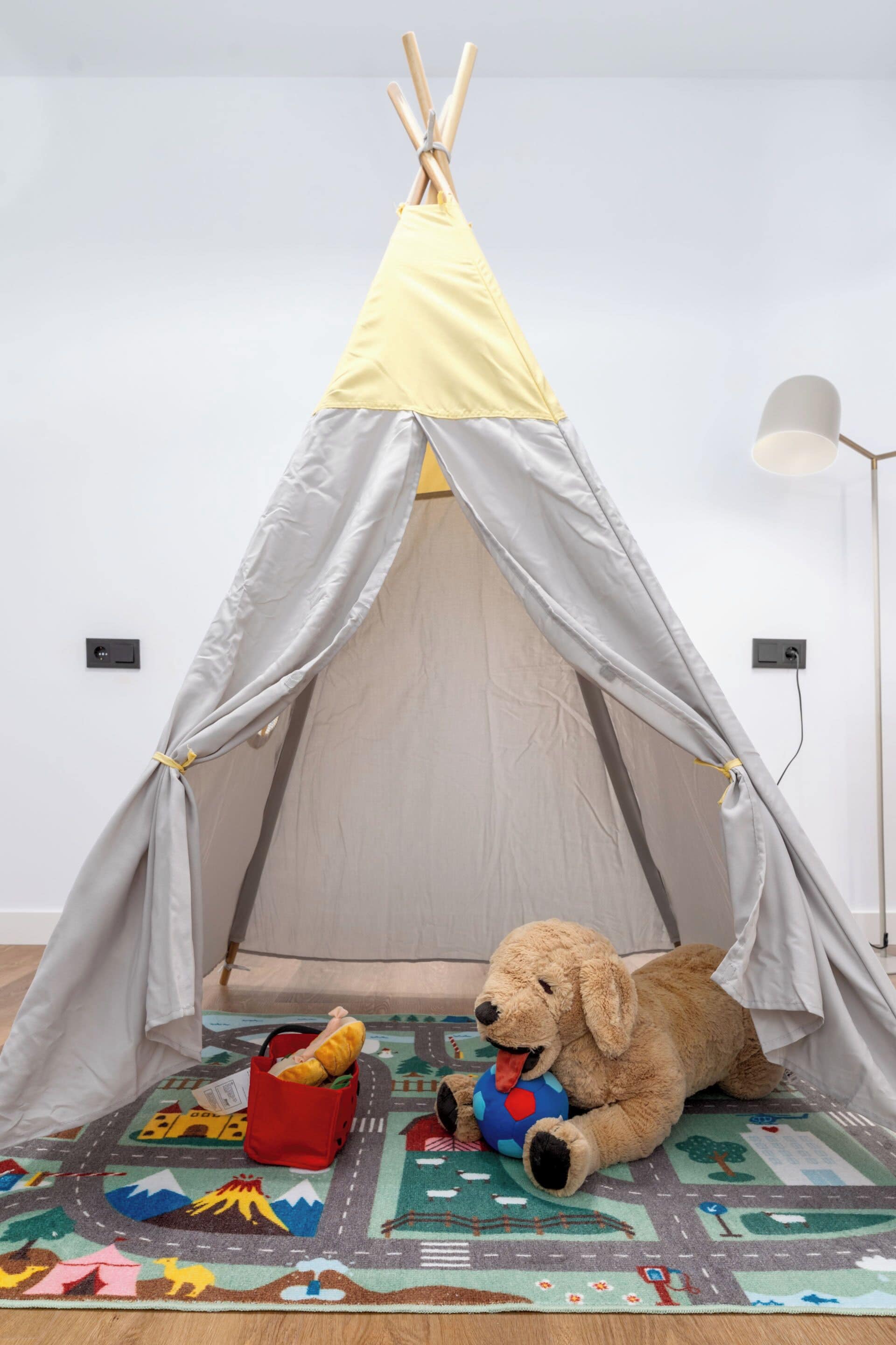 A tent with a sleeping bag inside, a stuffed dog, and a red basket on a patterned rug.