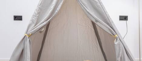 A tent with a sleeping bag inside, a stuffed dog, and a red basket on a patterned rug.