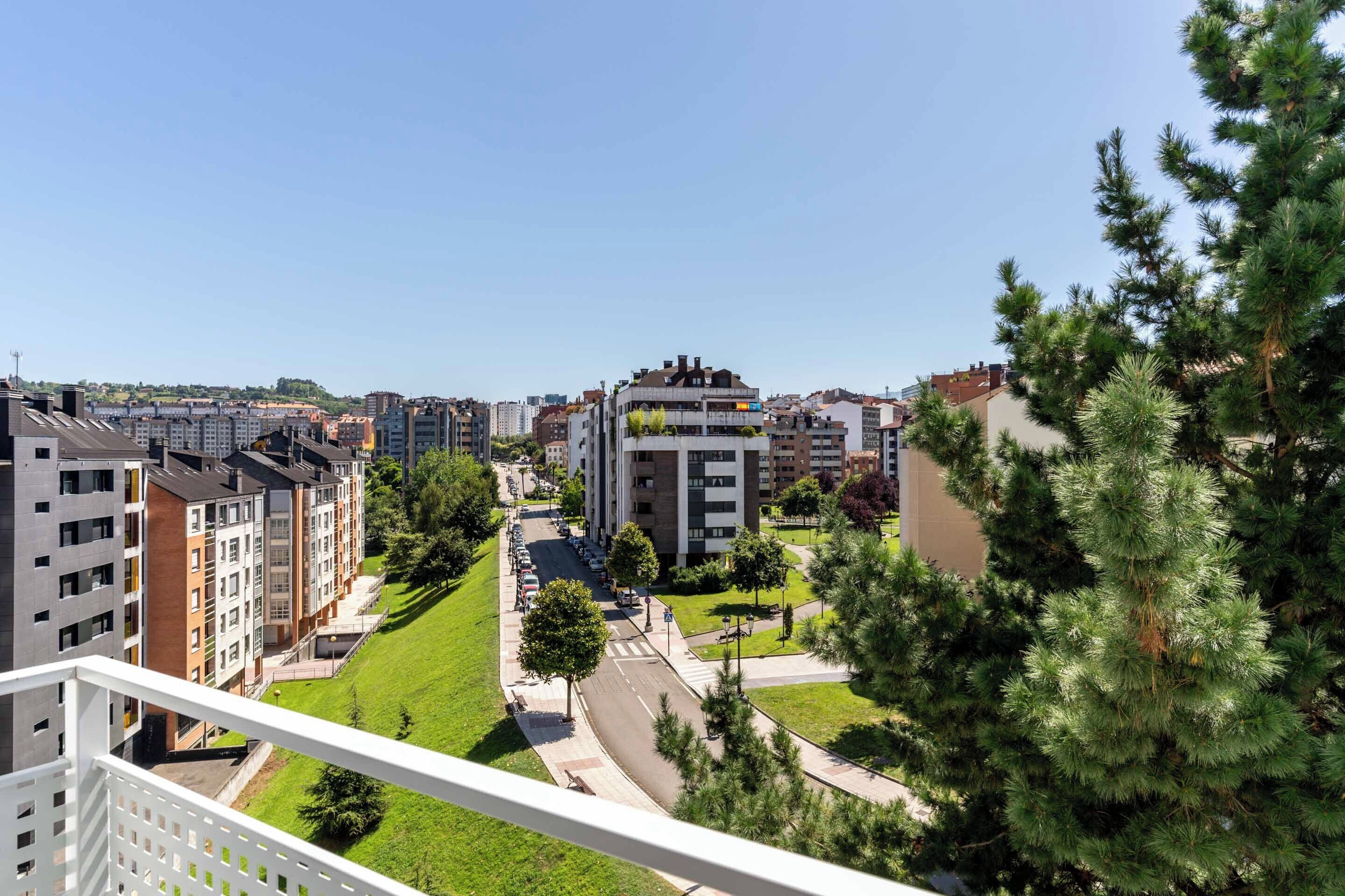 A residential area with modern apartment buildings, a green park, and a clear sky.