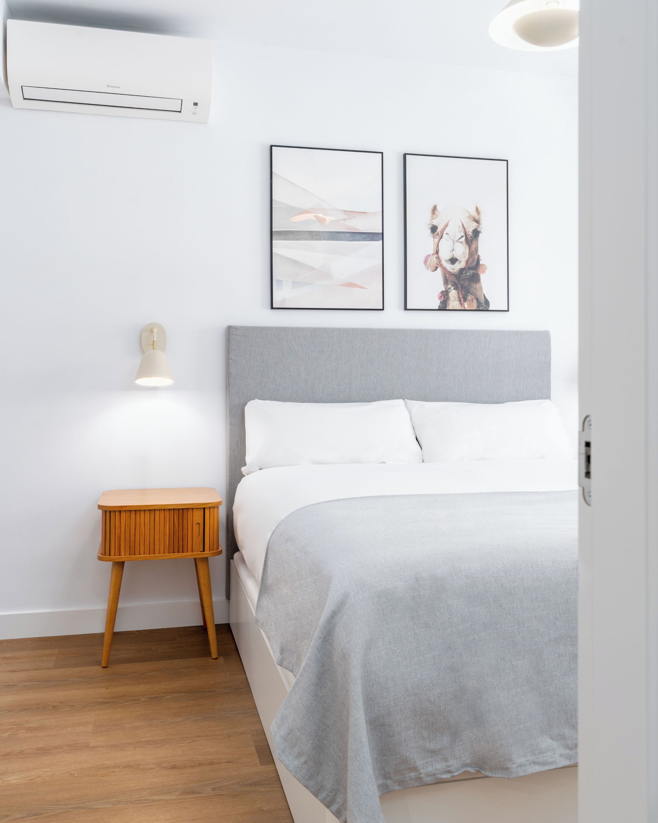Una camera da letto con un letto, un comodino, un condizionatore d'aria a parete e due quadri appesi.