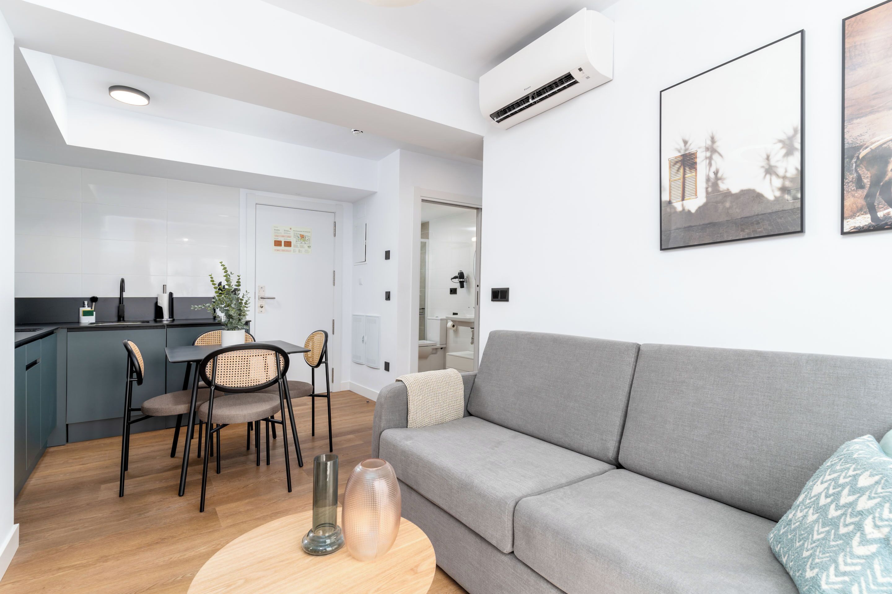 Ein modernes Wohnzimmer mit grauem Sofa, einem Essbereich mit Tisch und Stühlen sowie einer Küche im Hintergrund.