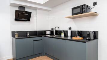 A modern kitchen with grey cabinets, a black countertop, a built-in microwave, and a coffee machine.