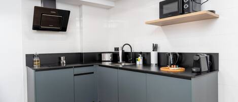 A modern kitchen with grey cabinets, a black countertop, a built-in microwave, and a coffee machine.