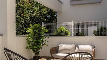 Un patio exterior con mobiliario de mimbre, una mesa redonda y una planta en maceta.