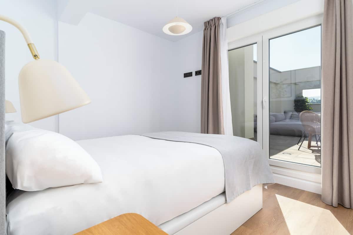 Une chambre moderne avec un lit, une lampe de chevet, une vue sur l’extérieur à travers une porte vitrée et un luminaire au plafond.