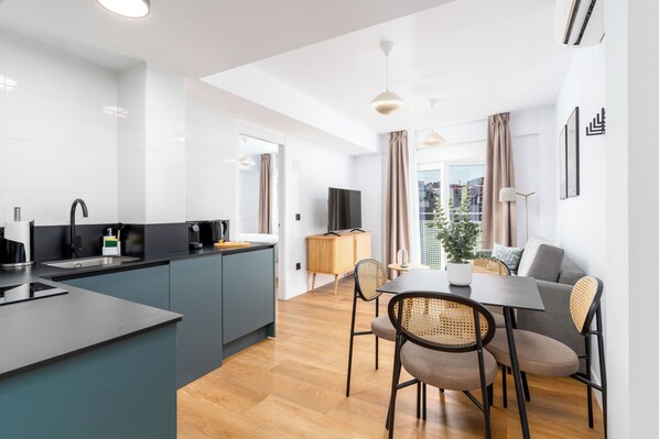 A modern kitchen with a central island, dining area with a table and chairs, and a view of the city through large windows.