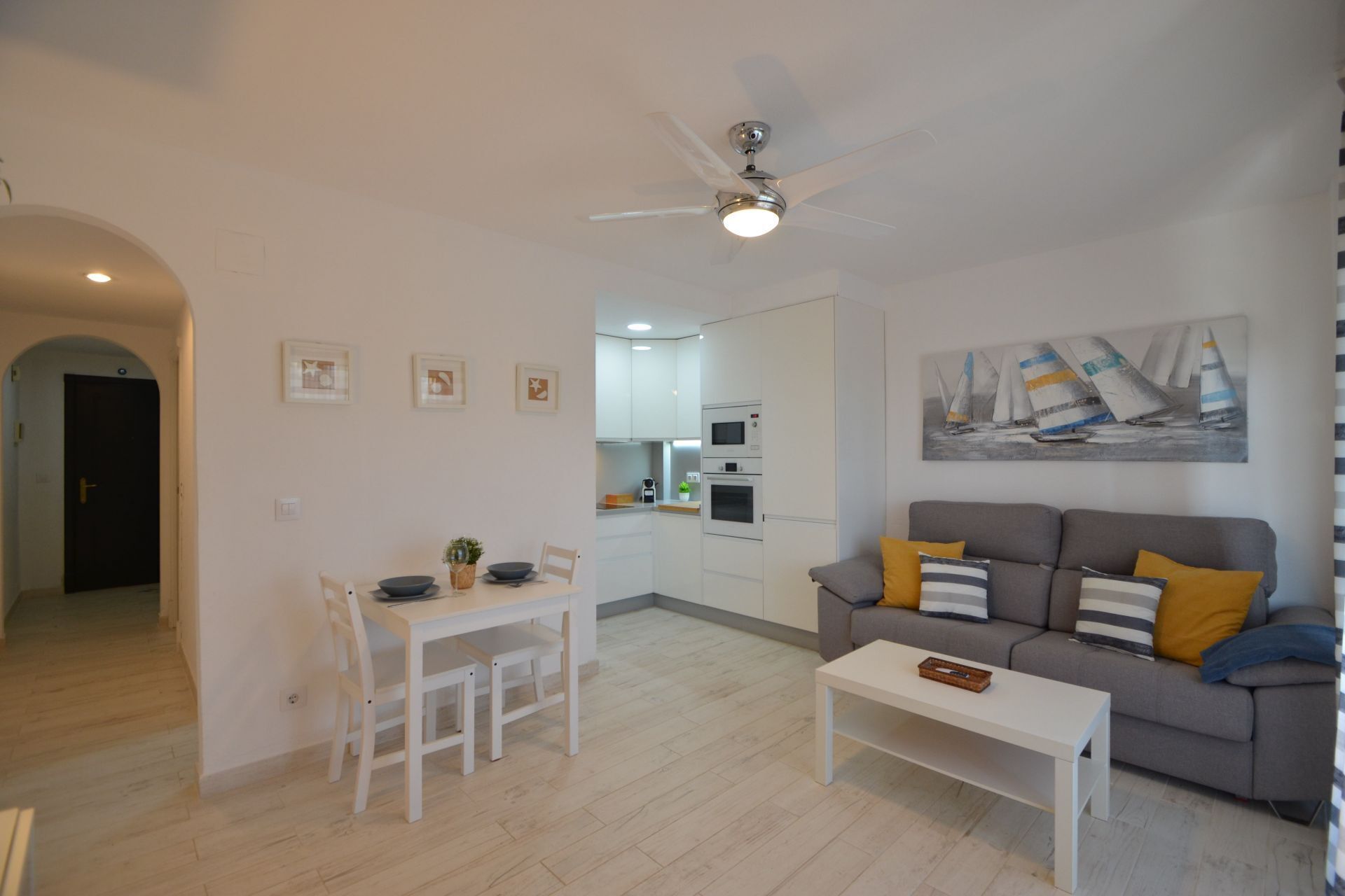 A modern living room with a grey sofa, white coffee table, and a dining area with white chairs and a table.