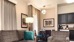 A hotel room with a patterned sofa set, a dining table with chairs, a kitchen area with cabinets, and a cityscape view through the window. - Explore San Diego right outside your door. (San Diego)