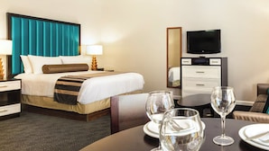 A hotel room with a bed, bedside tables, a TV, a dining table with glasses, and a chair. - Explore San Diego right outside your door. (San Diego)