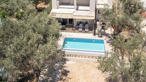 Una casa moderna de dos pisos con piscina, rodeada de árboles.