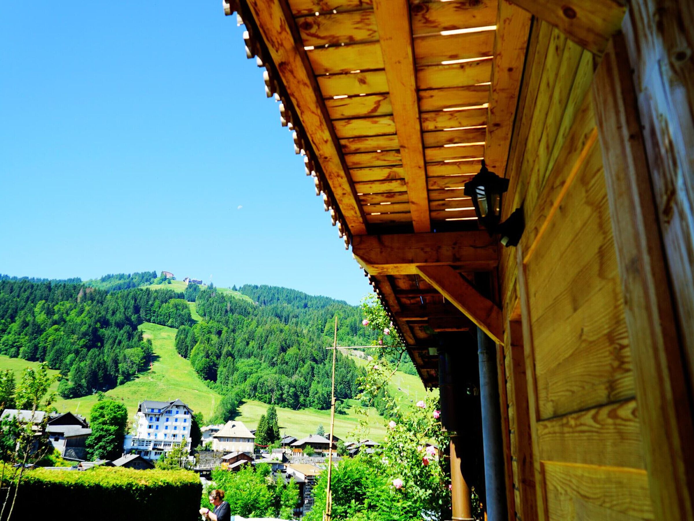 A wooden building with a view of a village and forested hills.