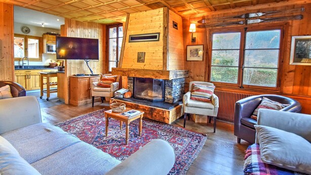 Interior acogedor de una cabaña con chimenea de piedra, paredes de madera y un ventanal con vistas al exterior.