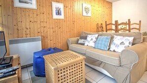 Una sala de estar acogedora con una pared de madera, un sofá con cojines estampados, un reposapiés azul y una silla de madera.