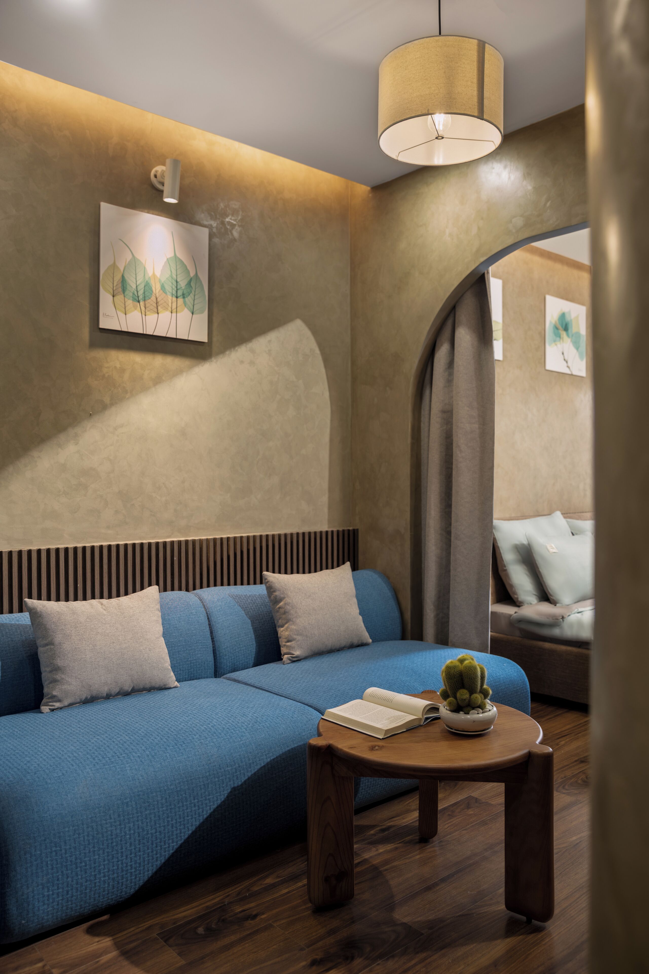 A modern living room with a blue sofa, a wooden coffee table with a book and a cactus, and a painting on the wall.