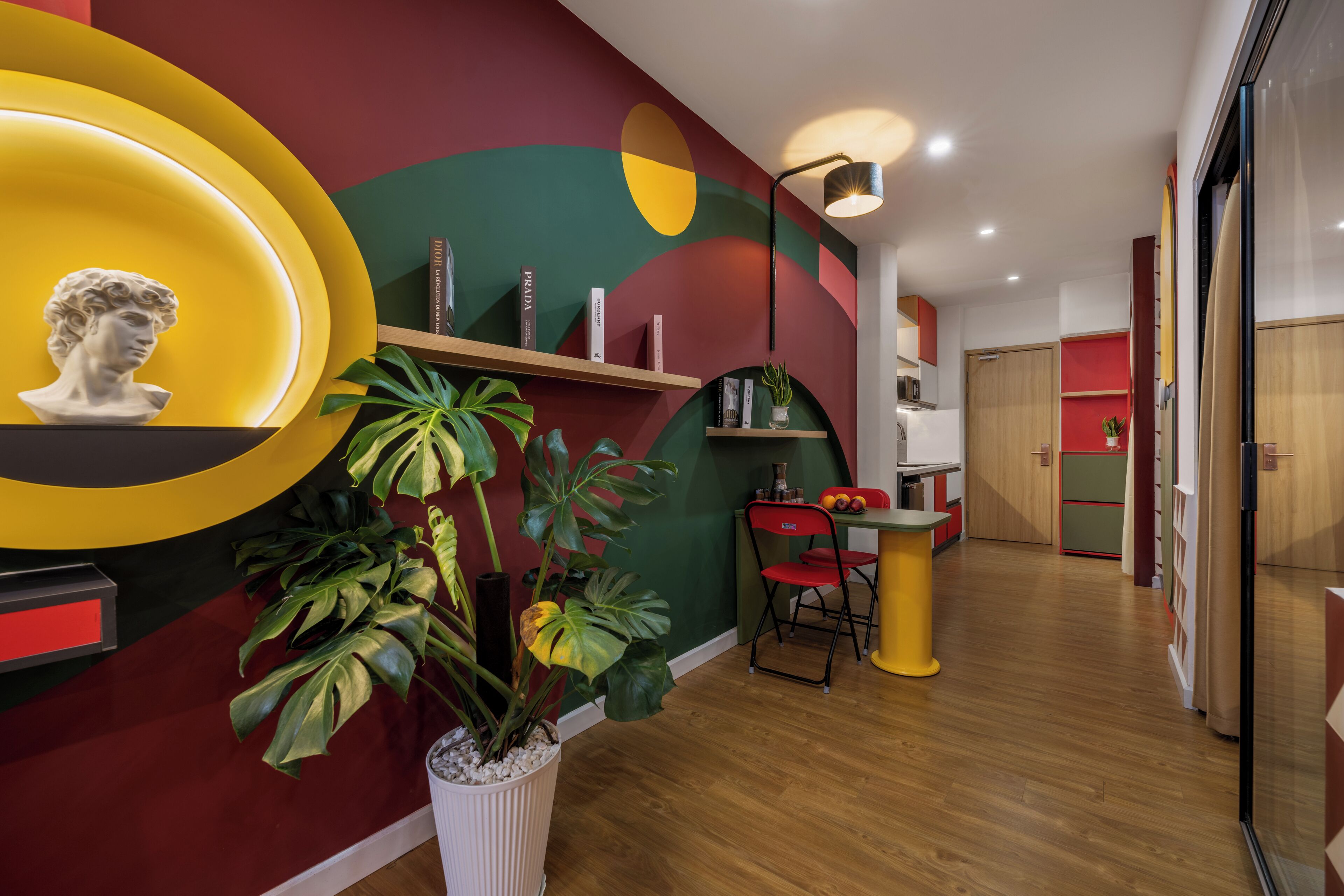 Un intérieur moderne avec un plancher en bois, un coin repas doté d’une table jaune et de chaises rouges, et un mur orné d’un grand motif abstrait.