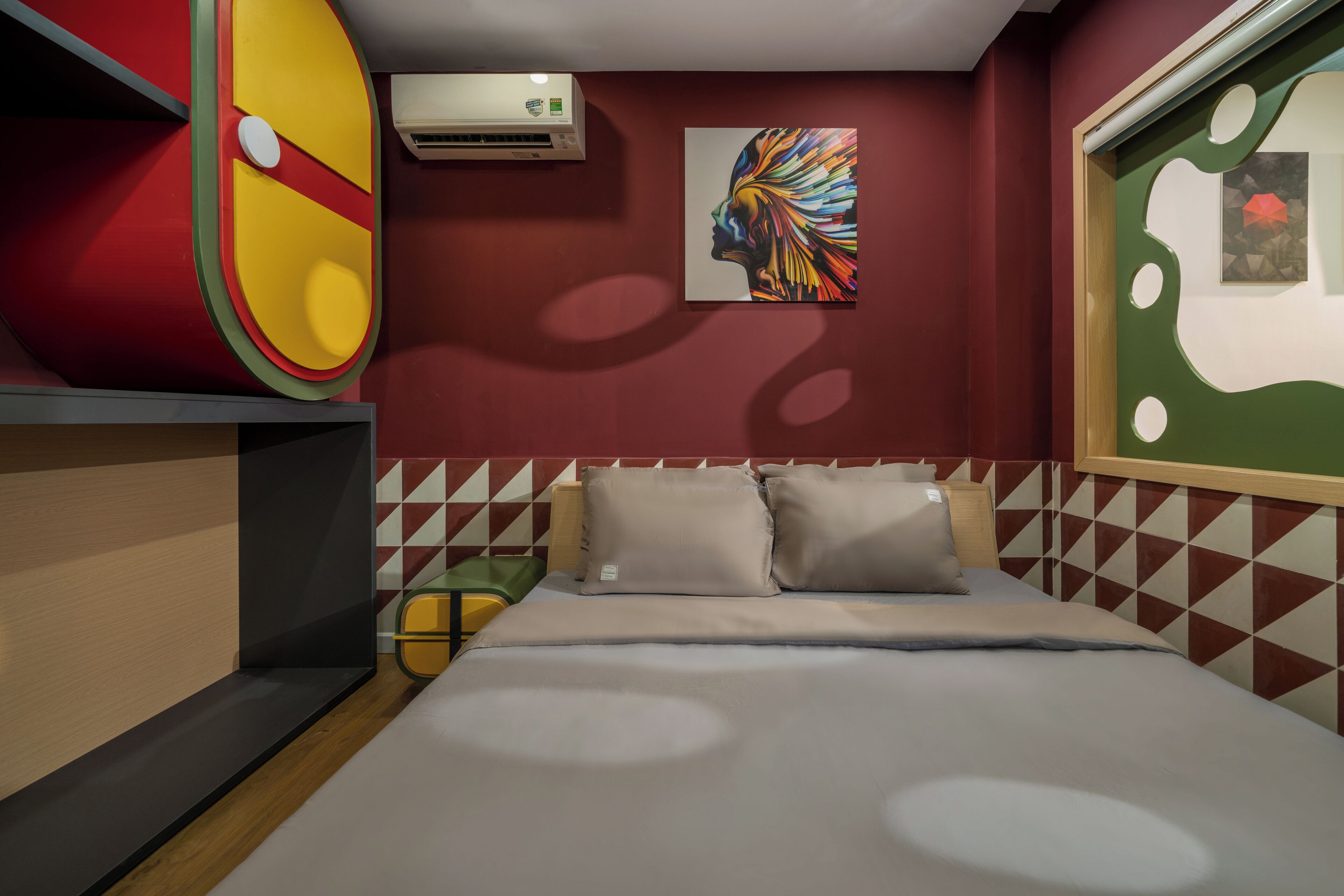 Une chambre d’hôtel avec un lit, des oreillers, un climatiseur fixé au mur et une œuvre d’art aux couleurs vives.