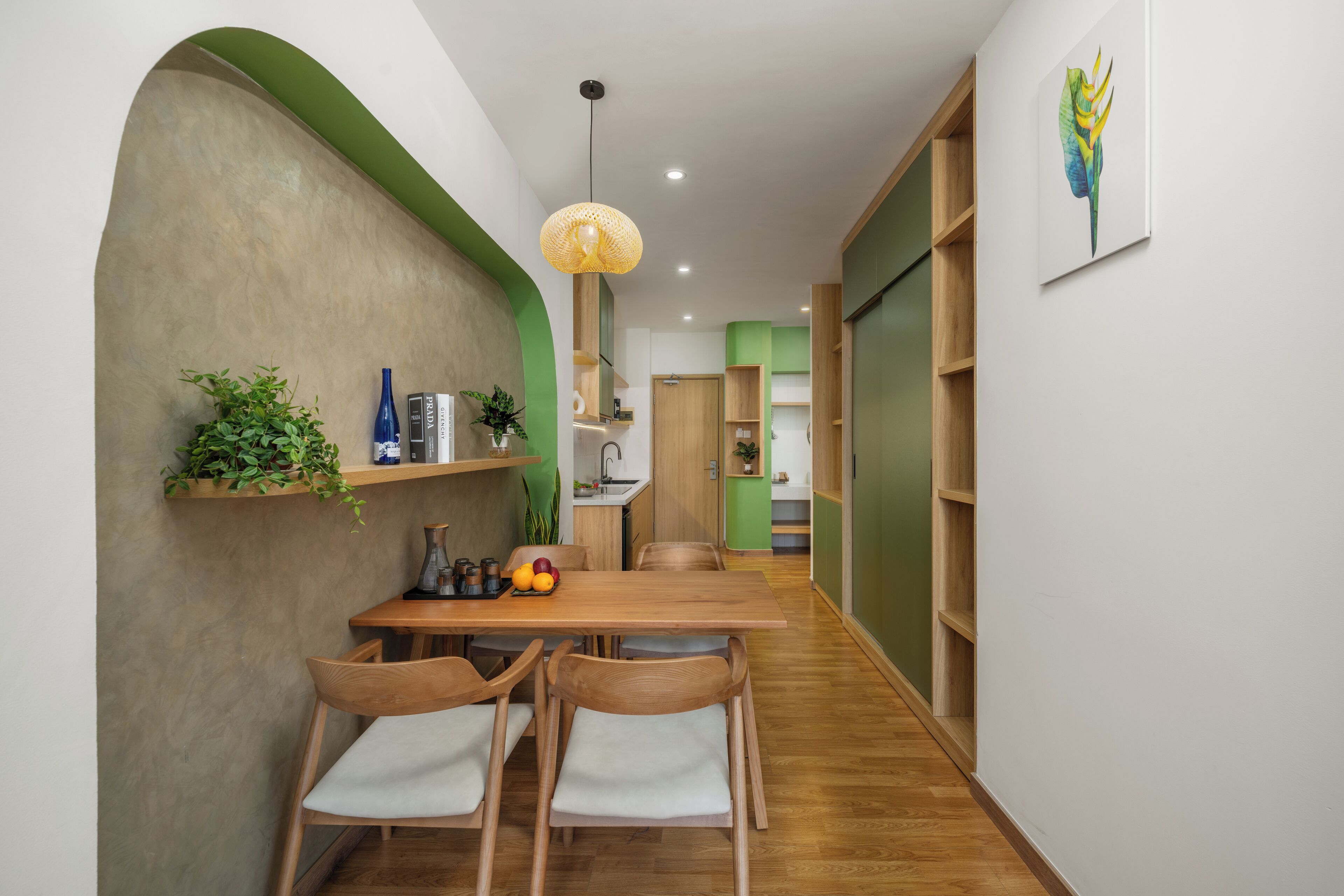 A modern dining area with a wooden table and chairs, a hanging light fixture, and a green accent wall.