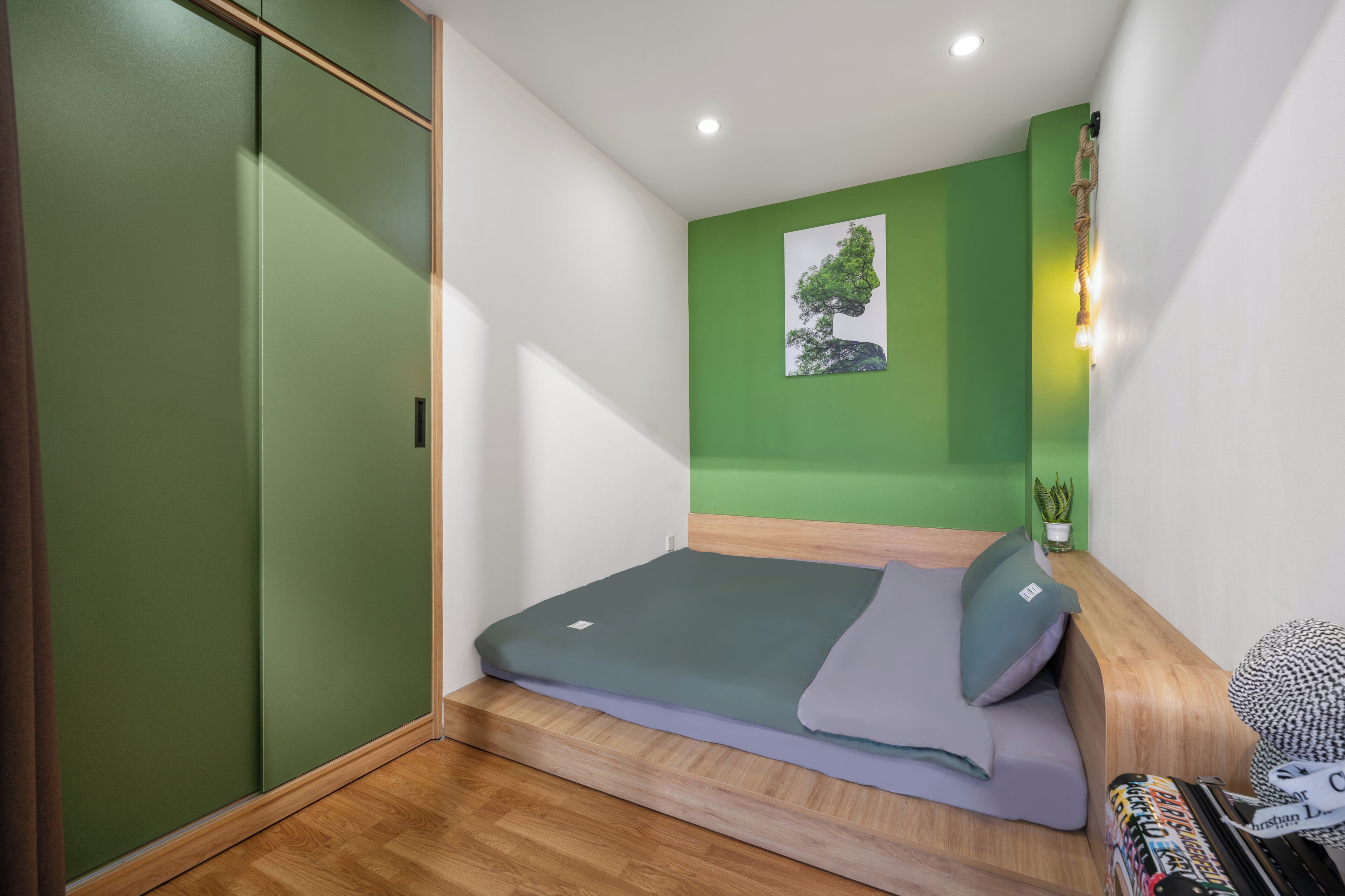 A bedroom with a bed, a green wall, a painting, and a small plant.