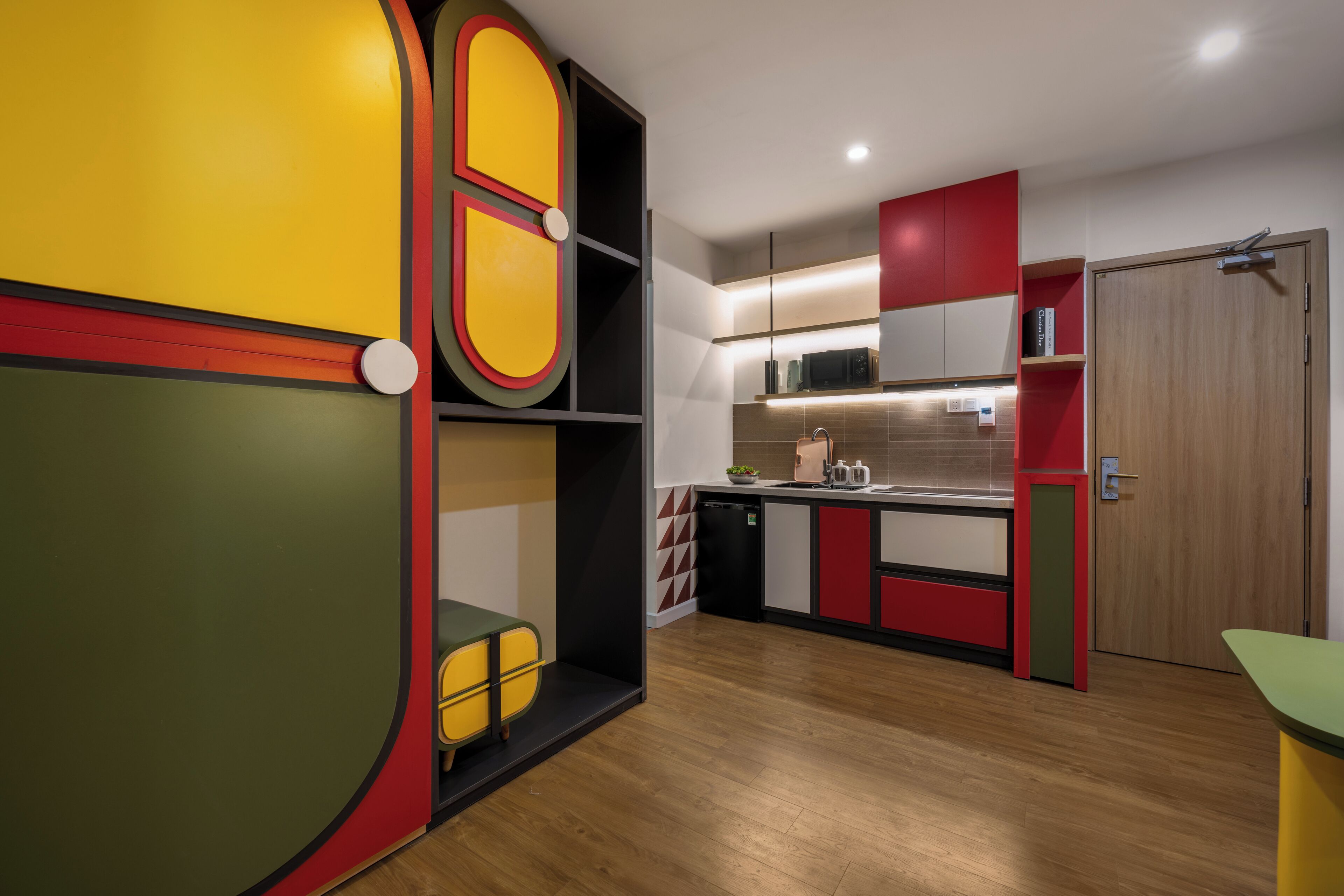 A modern kitchen with wooden flooring, red and yellow cabinets, and a microwave.