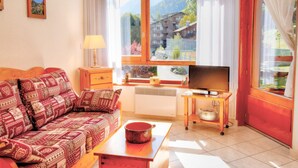 A cozy living room with a patterned sofa, a television, and a window with a mountain view. - Cozy studio near Morzine center for 4 ppl. (Morzine)
