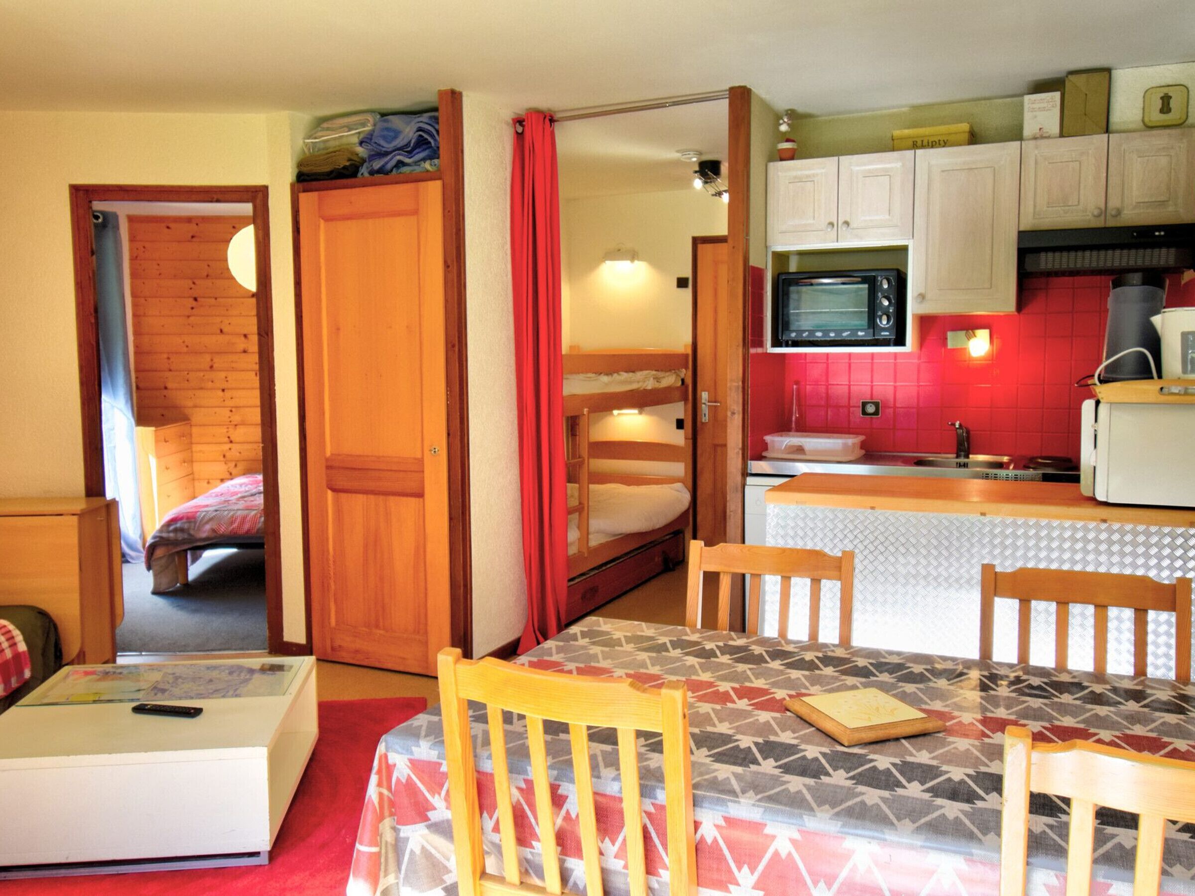 A compact kitchen with a microwave, sink, and wooden cabinets. There is a small dining area with a table and chairs.