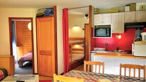 A compact kitchen with a microwave, sink, and wooden cabinets. There is a small dining area with a table and chairs.